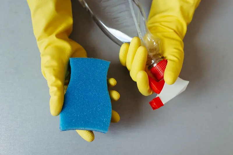 Yellow rubber gloves holding a sponge and a spray bottle, the basic gear for cleaning small mold spots in a Cary, NC home