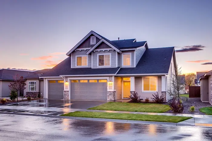 Two-story suburban house at dusk after rain, its driveway still wet